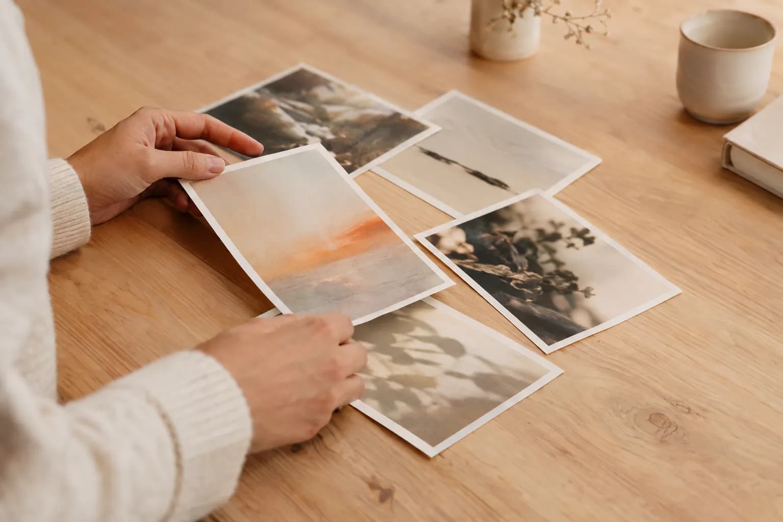 Mãos organizando fotografias impressas sobre uma mesa de madeira clara