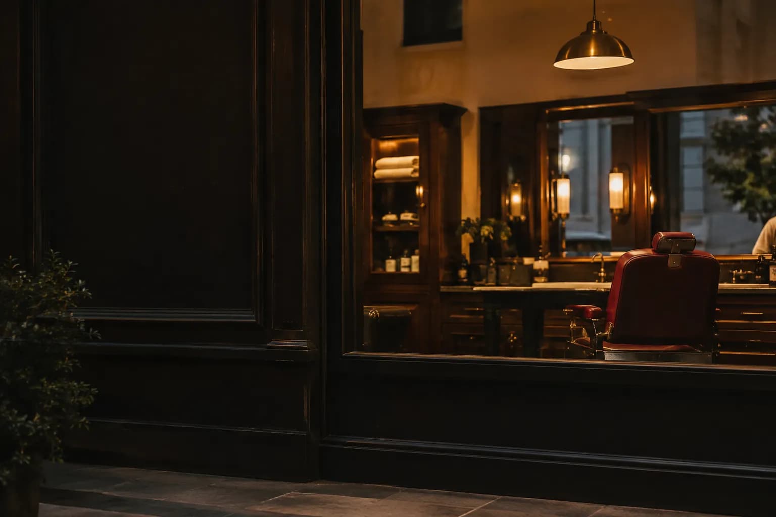 Vitrine de uma barbearia ao anoitecer, com uma cadeira de couro iluminada por dentro